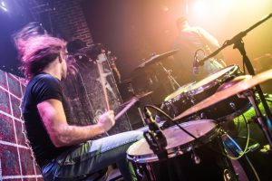 Drummer playing on drum set on stage. Warning - Focus on the drum, authentic shooting with high iso in challenging lighting conditions. A little bit grain and blurred motion effects.