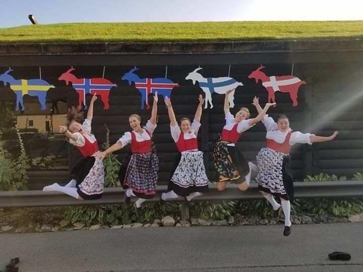 Fem kvinner i norske bunader hopper i luften under folkedans